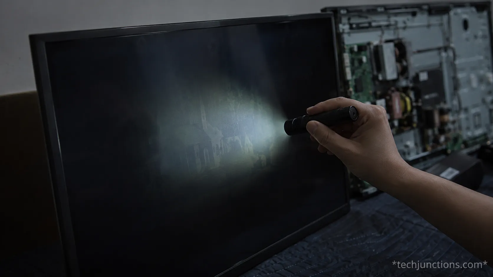 Flashlight test on a dark Sony Bravia screen with the back panel open on a repair bench.