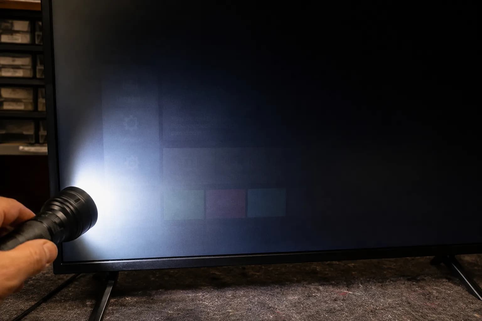 Flashlight shining at a 45-degree angle on a dark TV screen reveals a faint on-screen menu, confirming a failed LED backlight while the LCD panel is still working.