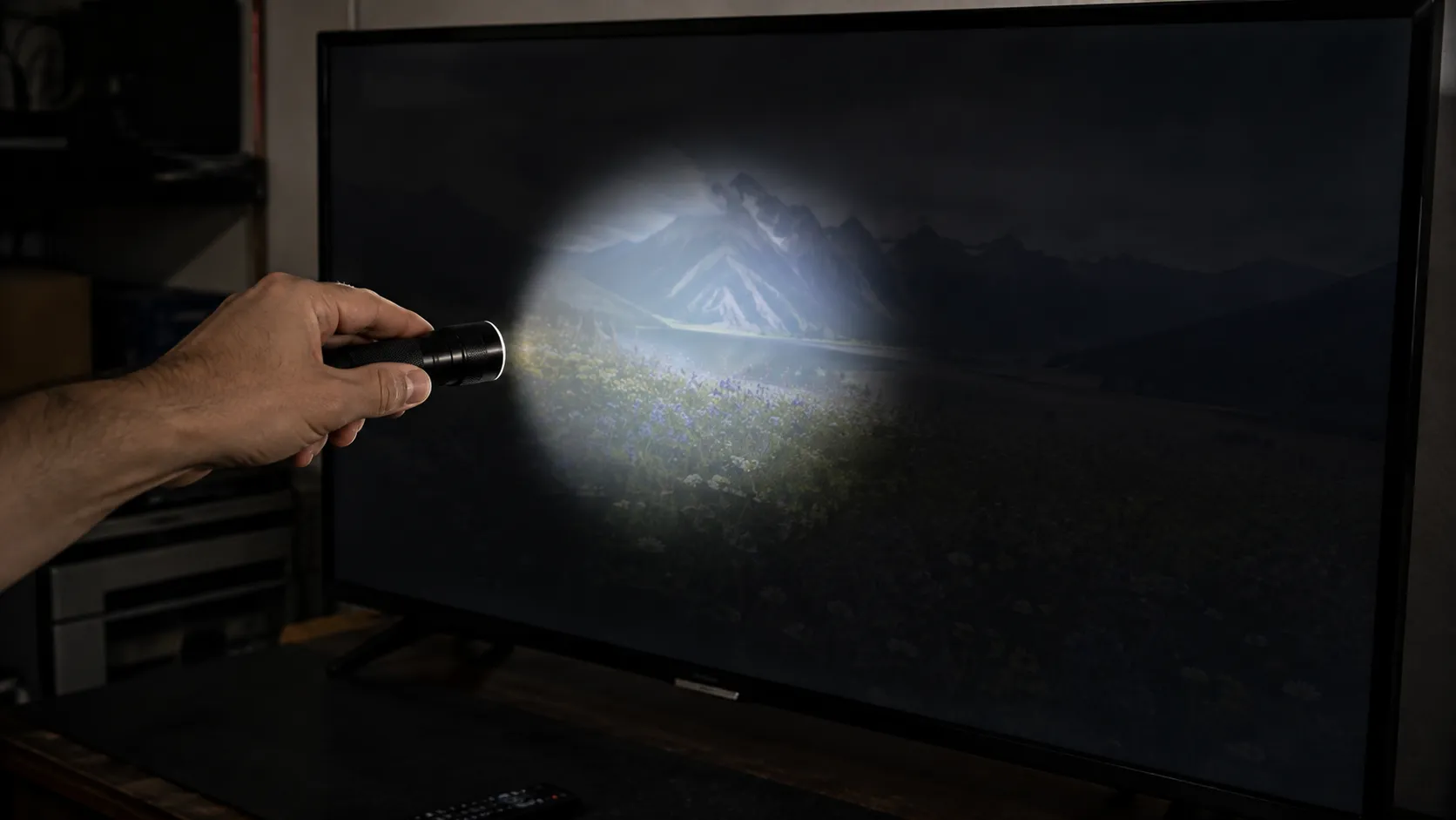 A hand shining a flashlight on a dark TV screen revealing a faint image, indicating a backlight fault.