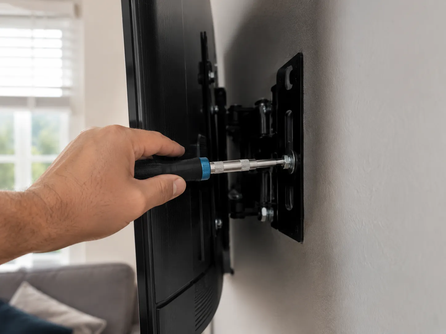 hand snugging a TV wall-mount bracket bolt to spec with a torque-limiting screwdriver to prevent screen cracking.