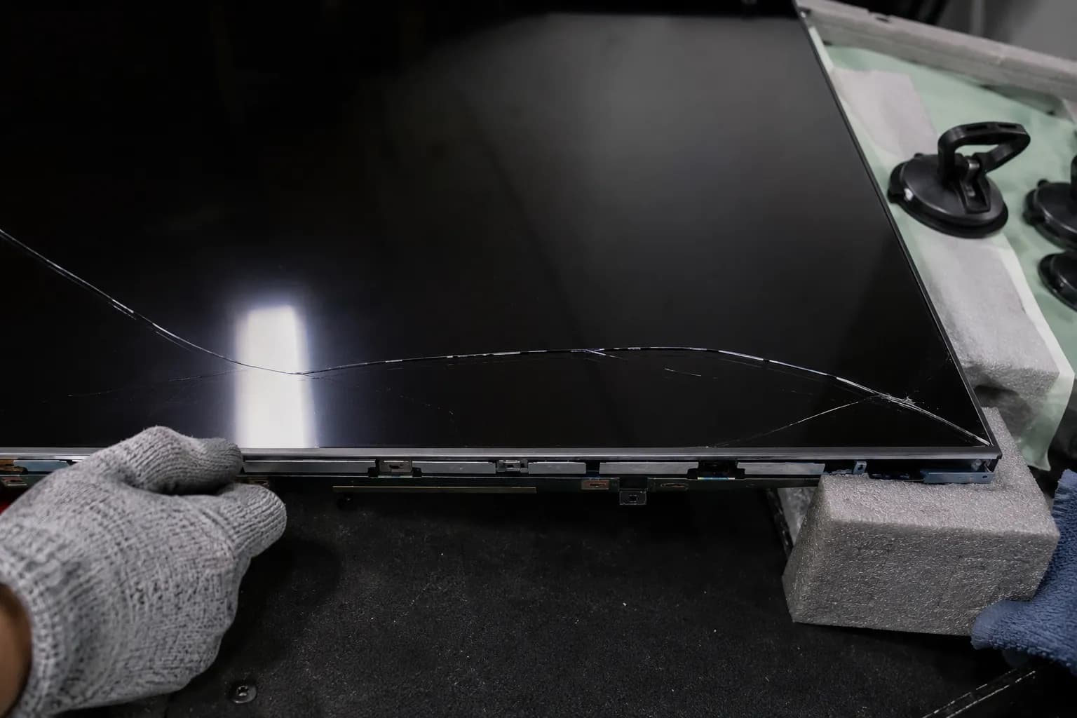 Bare replacement TV panel with a fresh crack across the glass during a DIY installation.