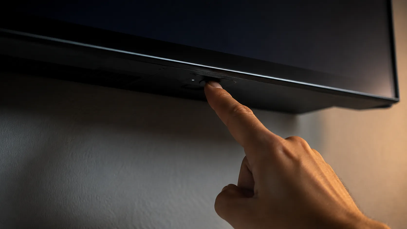 Close-up of the physical power button underneath an LG C3 OLED TV with a finger pressing it, illustrating how to discharge residual power during troubleshooting.