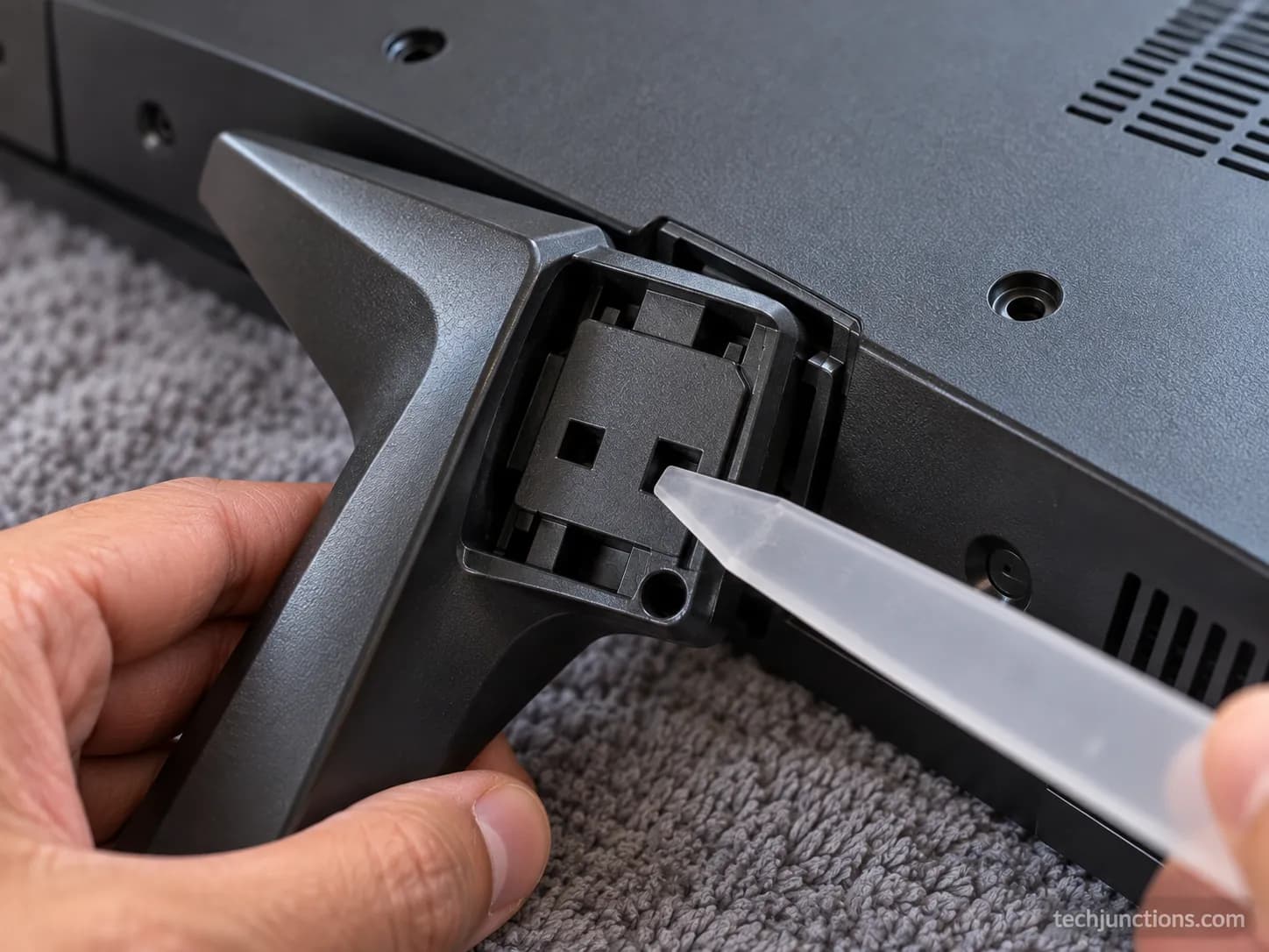 Thin plastic tool releasing an LG clip-in stand foot through its square hole during no-screw removal.