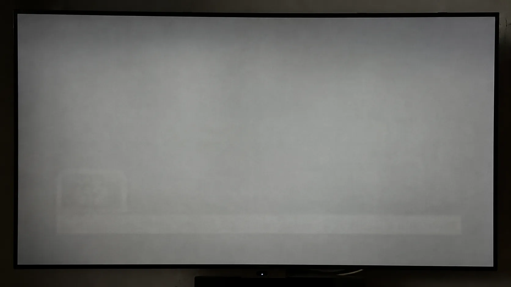 LG OLED TV displaying a grey test slide with faint burn-in from a retained news ticker and logo after extended use, demonstrating OLED image retention on an aging display.
