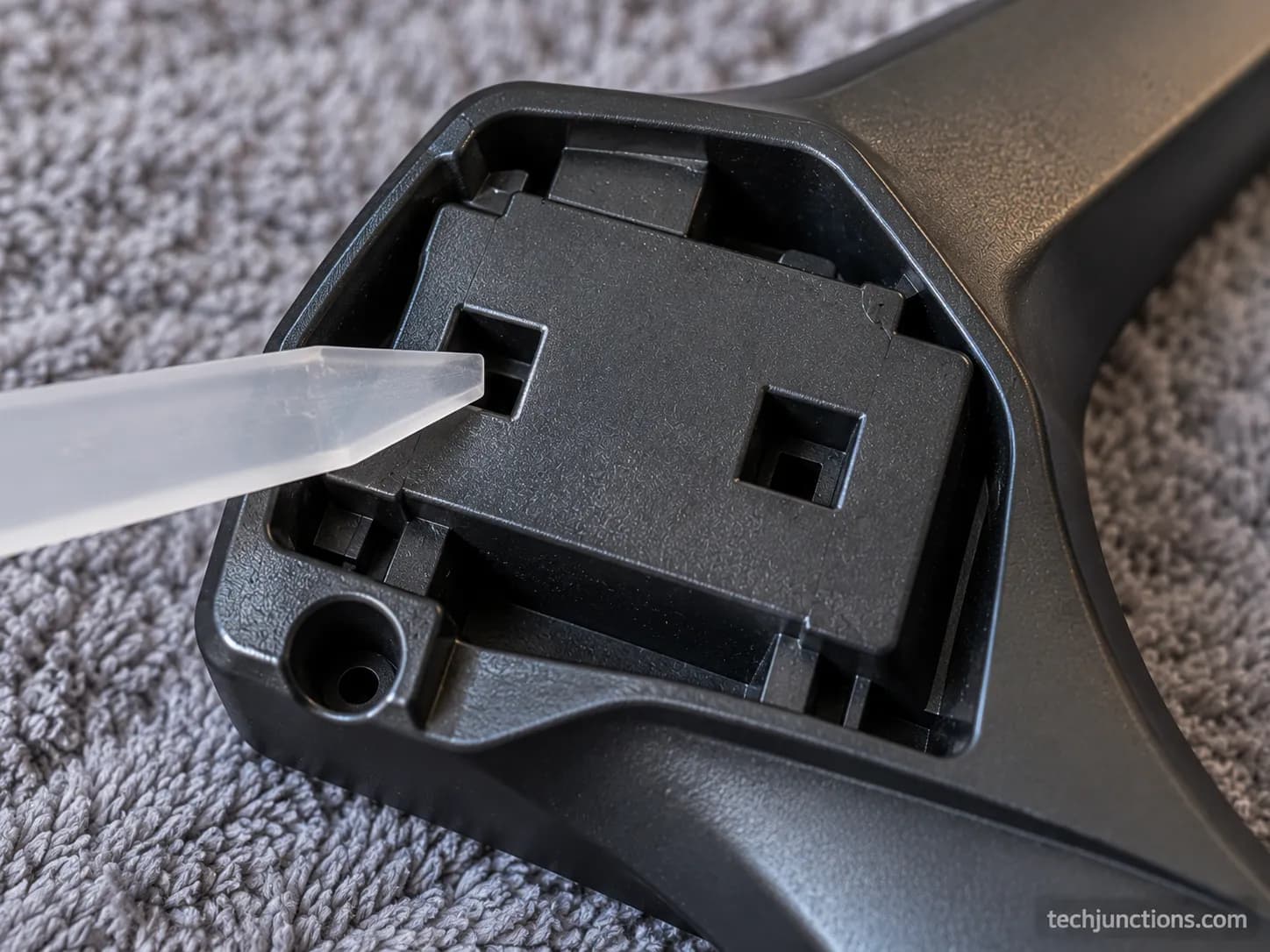 Underside of an LG clip-in TV stand foot showing two square release holes and no screws, with a plastic pry tool