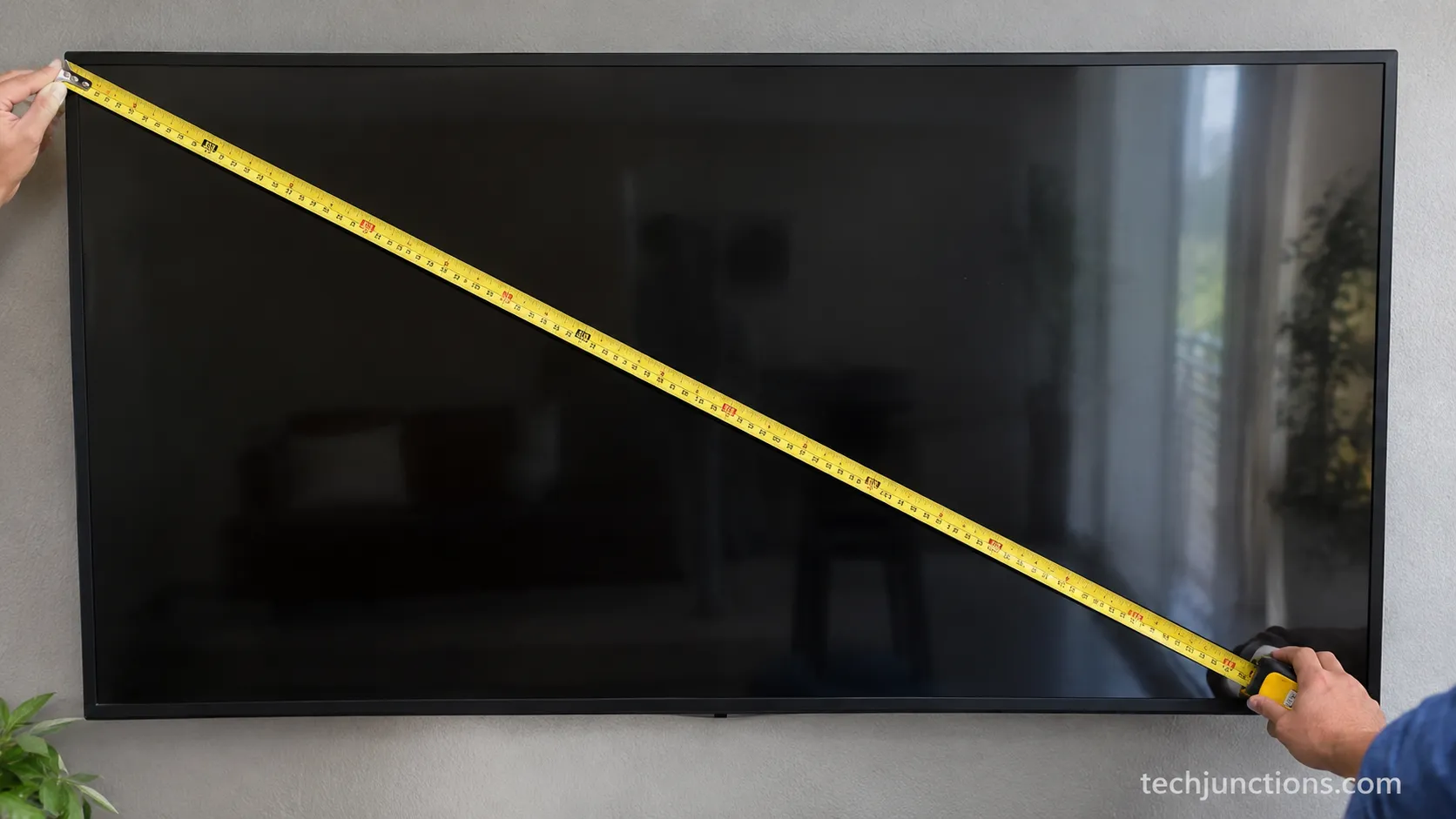 Measuring a television screen diagonally with a steel tape measure.