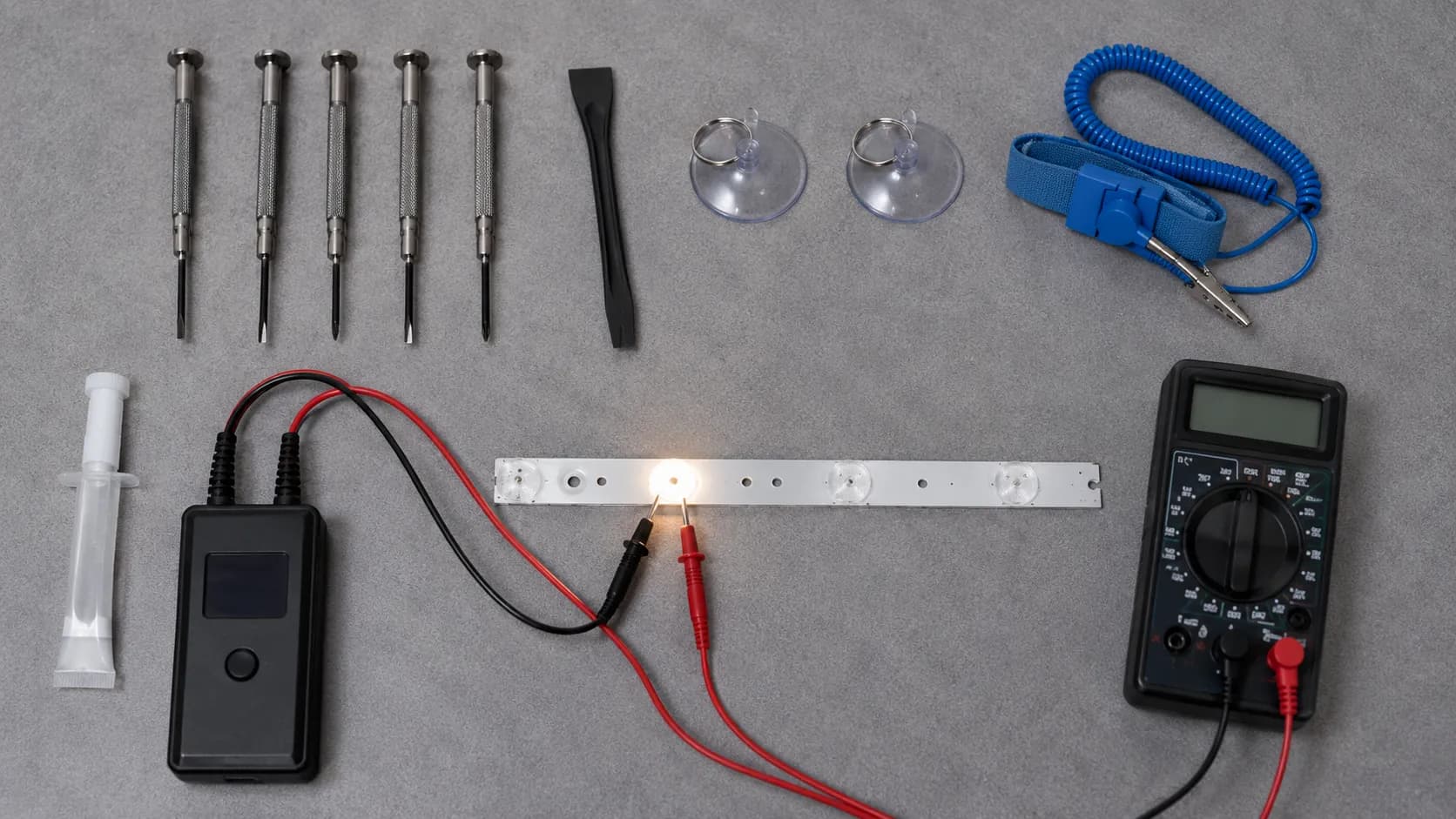 Flat-lay of a TV backlight repair toolkit with screwdrivers, multimeter, suction cups, anti-static wrist strap, adhesive, and an LED backlight tester powering a single LED strip.
