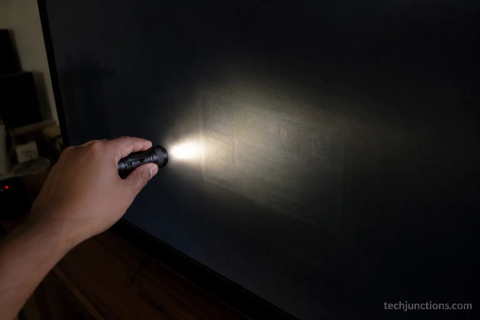 Flashlight held at an angle to a dark TV revealing a faint image, indicating a dead backlight rather than a broken panel.
