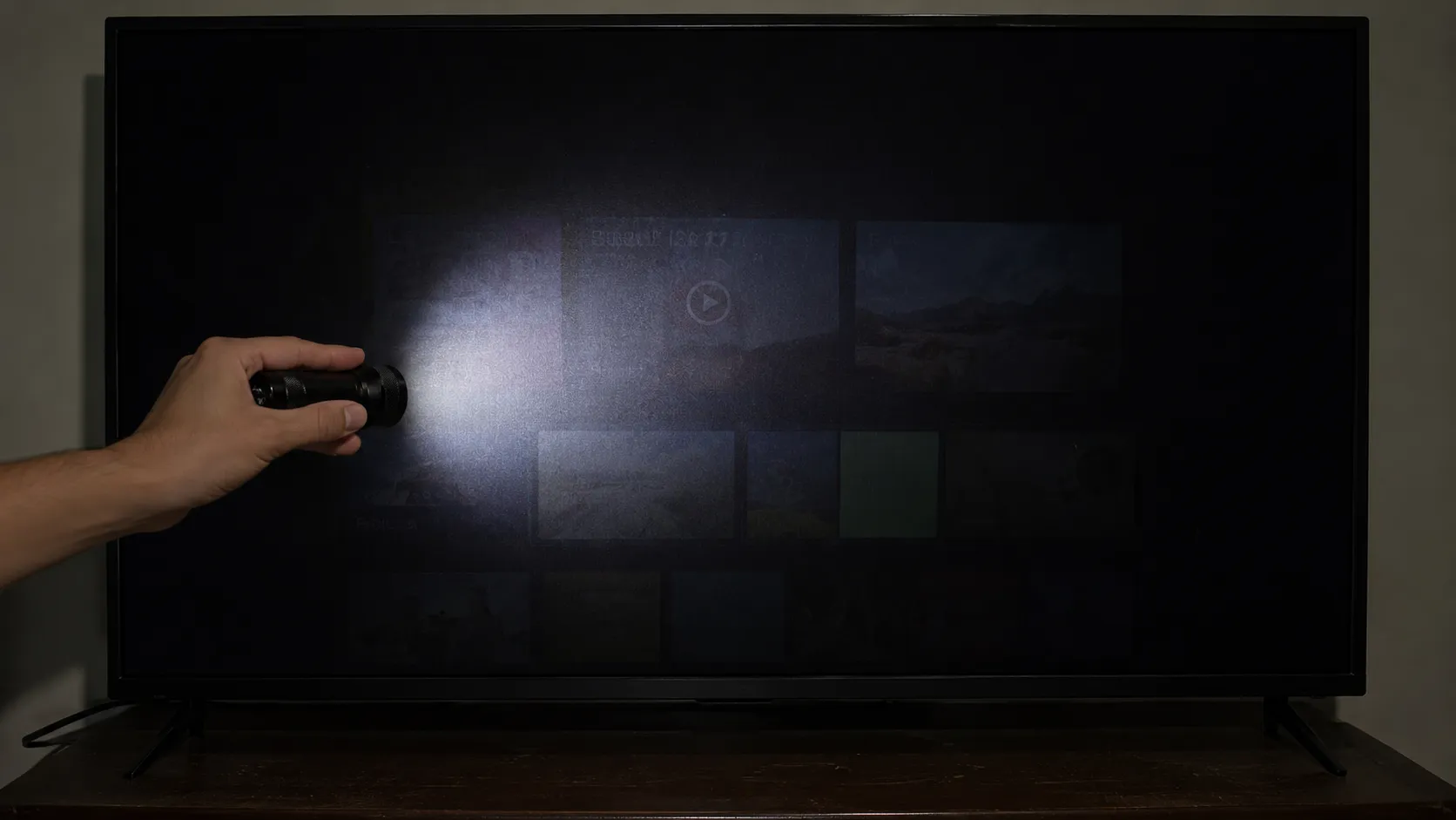 Flashlight test on a TV with a black screen revealing a faint home screen image, indicating the display works but the backlight may have failed.