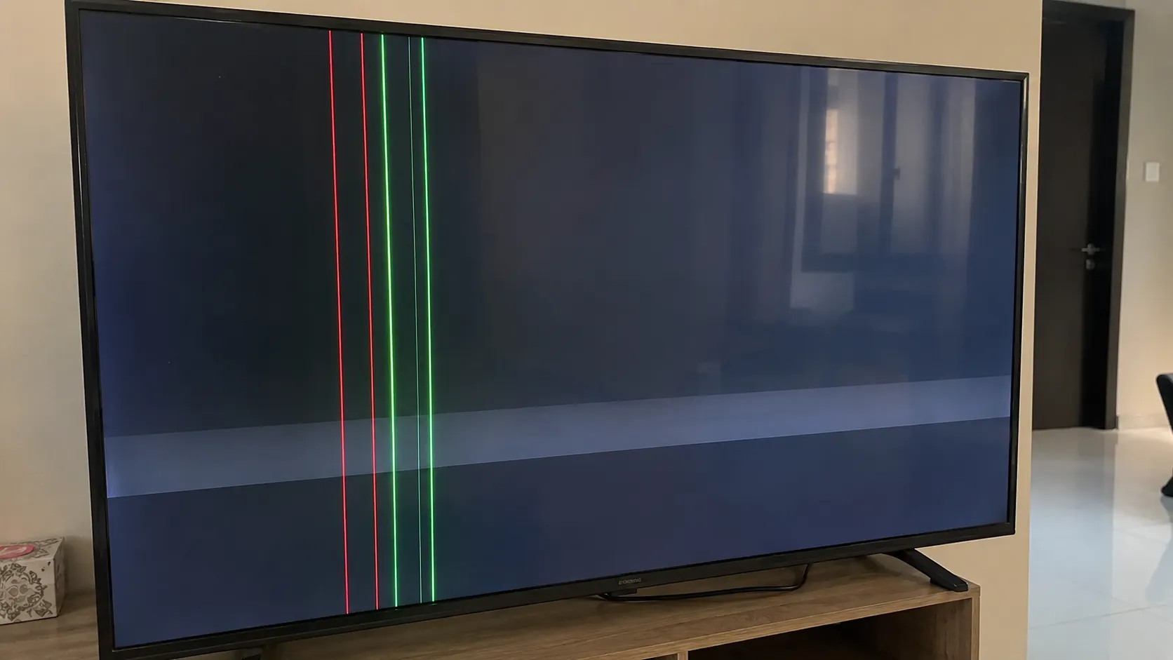 Close-up of a flat-screen TV showing vertical red and green lines with a faint horizontal band, illustrating a common display panel fault that often makes TV replacement more practical than repair.